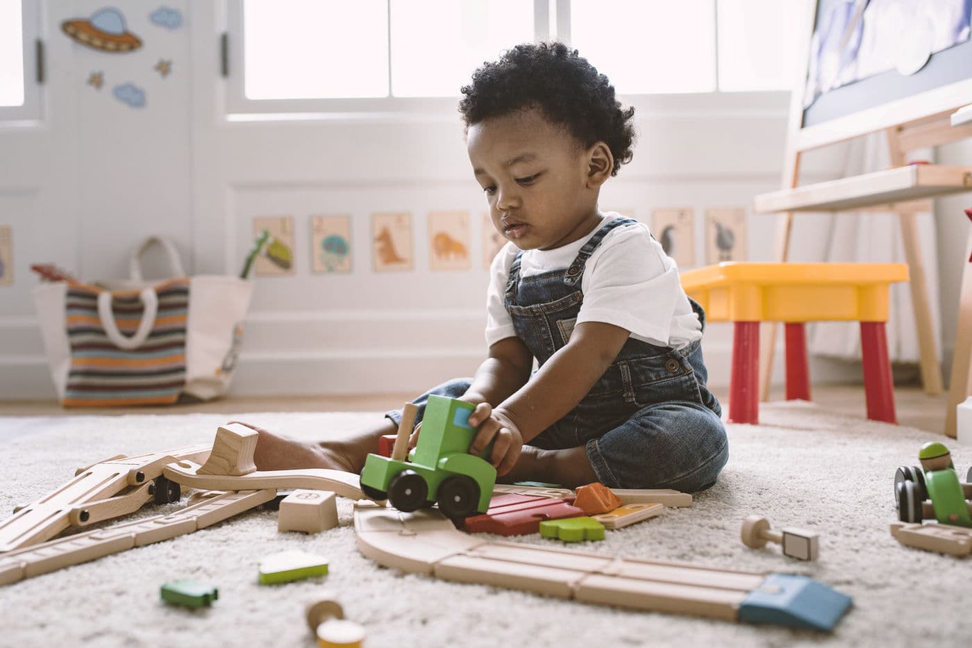A child playing with a wooden train on a soft rug
